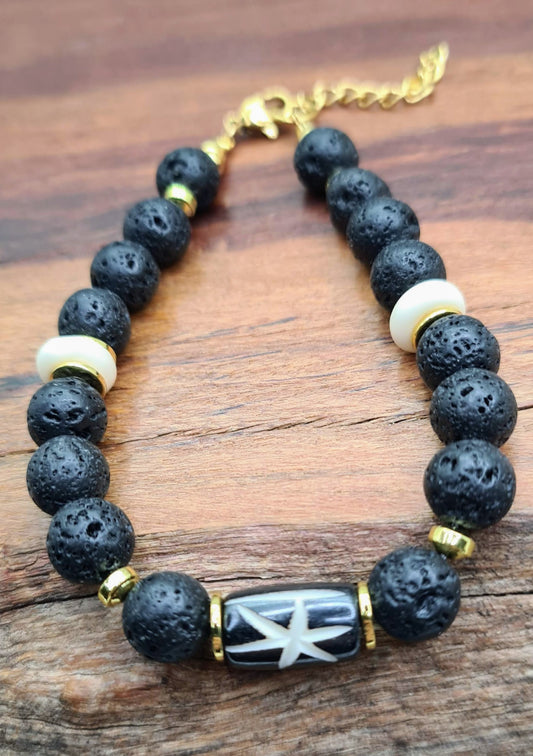 Pulsera masculina de cuentas de lava negra con pieza central de hueso tallado y separadores dorados sobre madera.