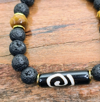 Detalle de pulsera masculina con lava volcánica negra, hueso de yak pintado, ojo de tigre facetado y separadores dorados.