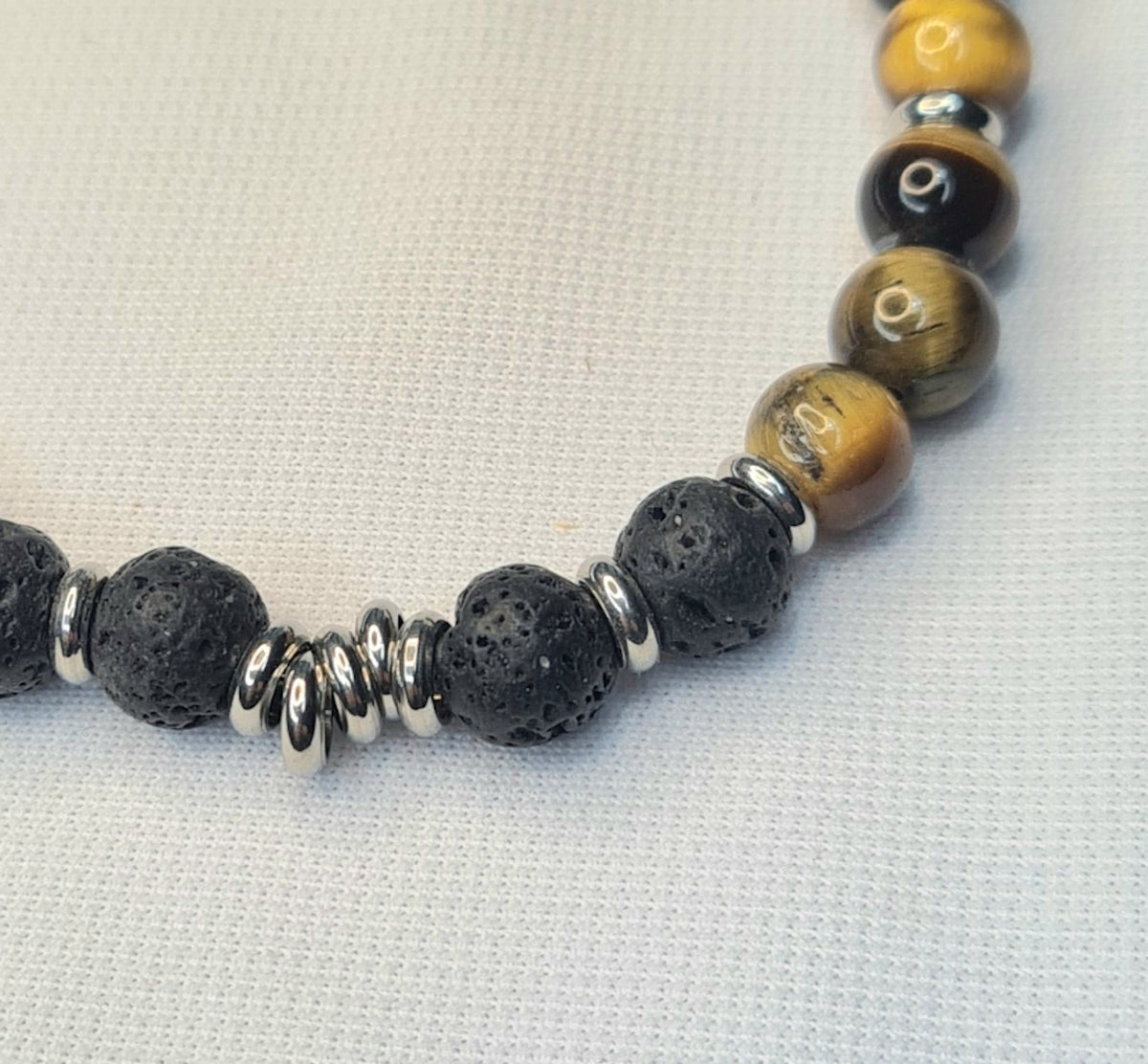 Detalle de pulsera de lava negra y ojo de tigre con varias anillas decorativas entre las cuentas.
