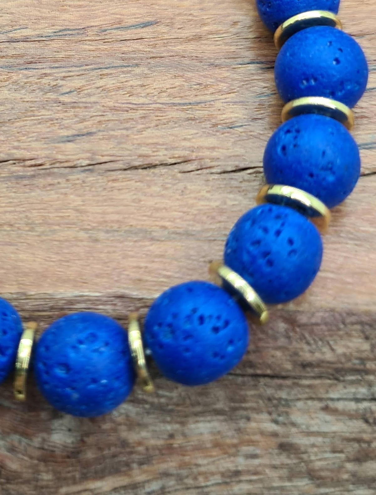 Detalle de cuentas de lava azul de superficie porosa con discos dorados.