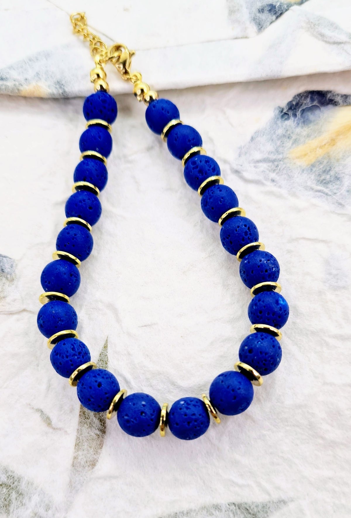 Pulsera de cuentas de lava azul con textura porosa y discos dorados.