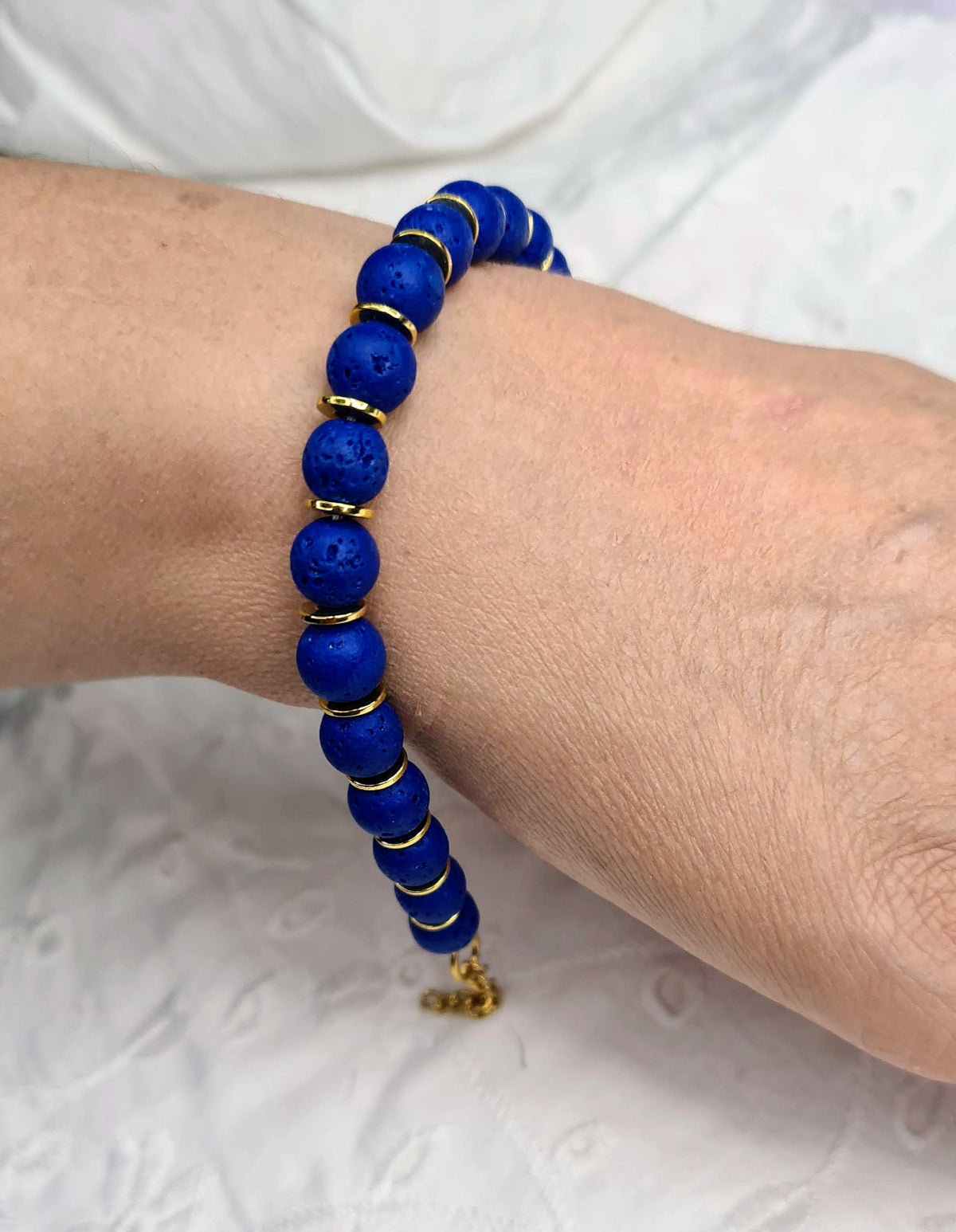 Pulsera de cuentas de lava azul con textura porosa y discos dorados.