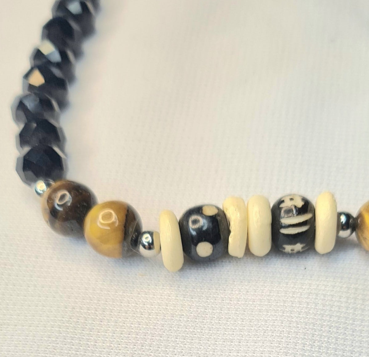 Detalle de pulsera con cuentas negras facetadas, ojo de tigre marrón y piezas de hueso de yak tallado.