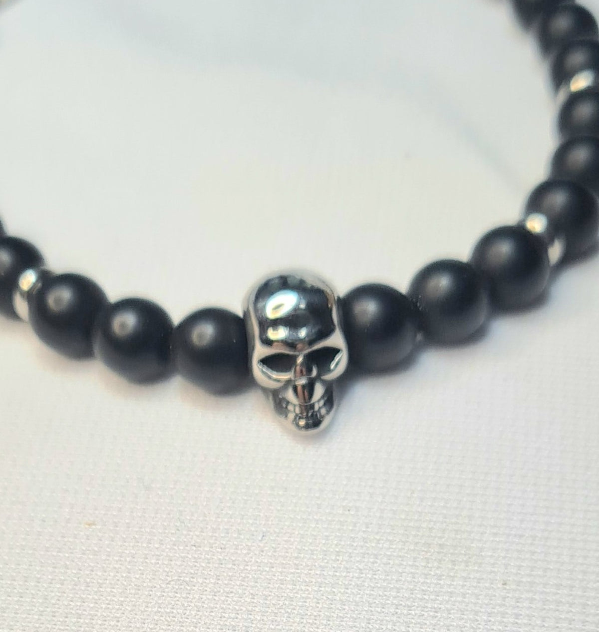 Primer plano de pulsera de ónix mate con figura central de calavera de acero.
