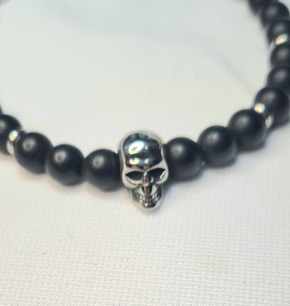 Primer plano de pulsera de ónix mate con figura central de calavera de acero.
