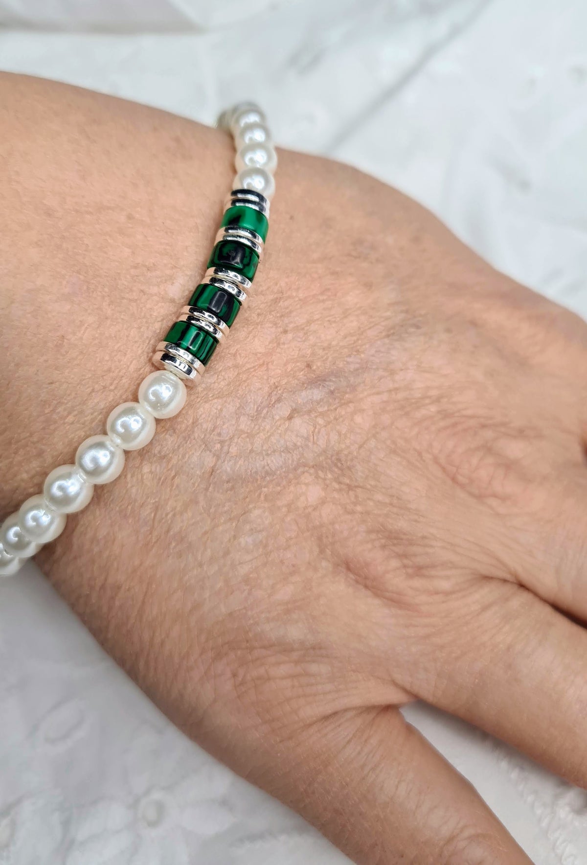 Pulsera de perlas con malaquita verde y detalles plateados puesta en una mujer.