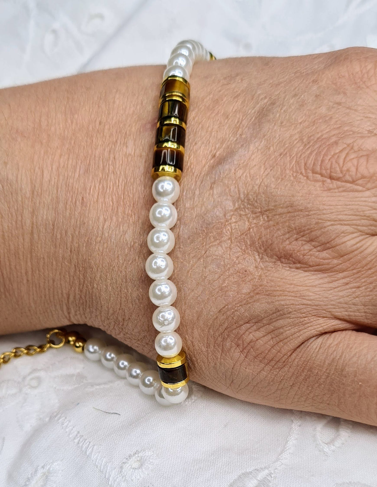 Pulsera de perlas con ojo de tigre y detalles dorados puesta en una mujer.