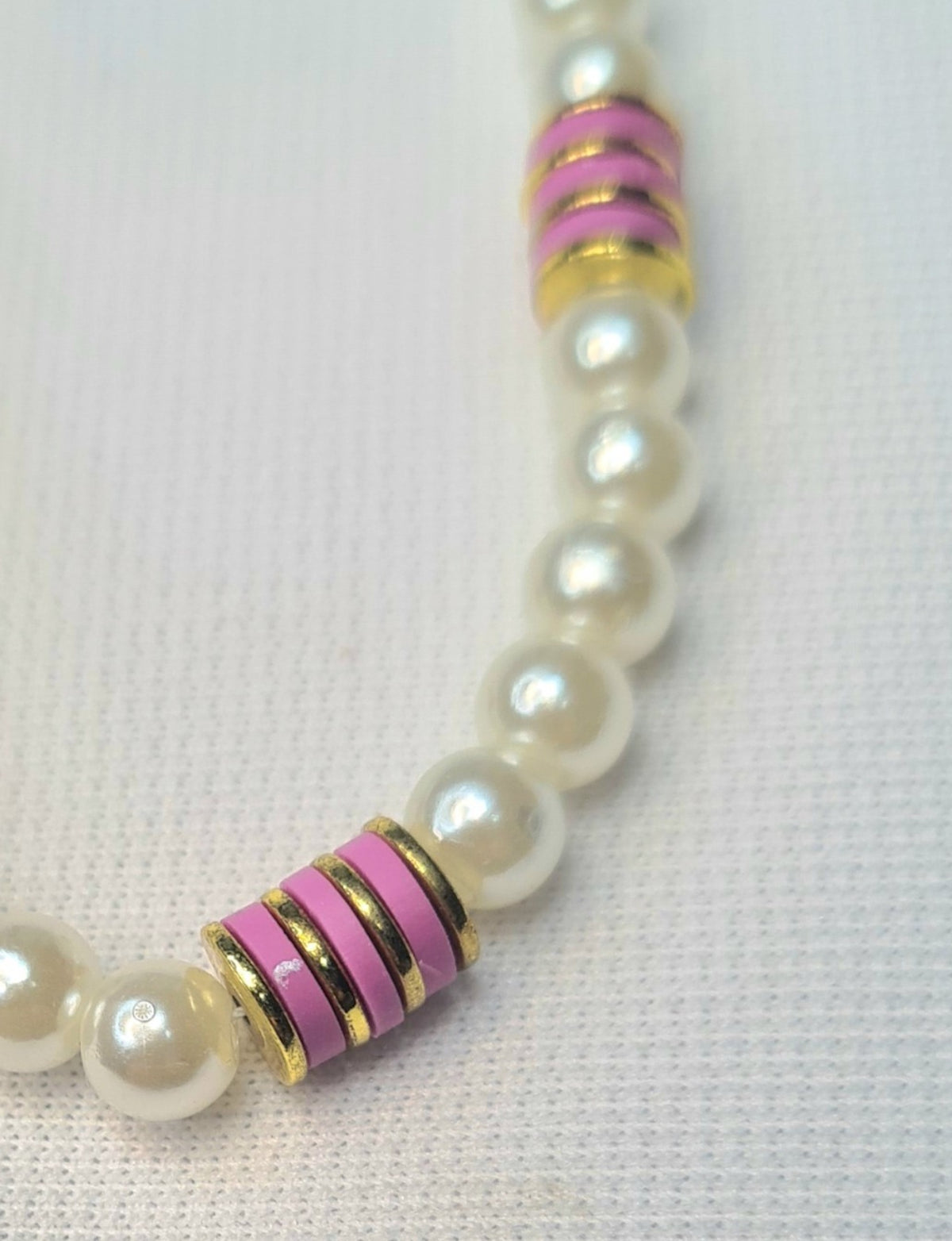 Detalle de pulsera de perlas con discos de cerámica rosa y separadores dorados.