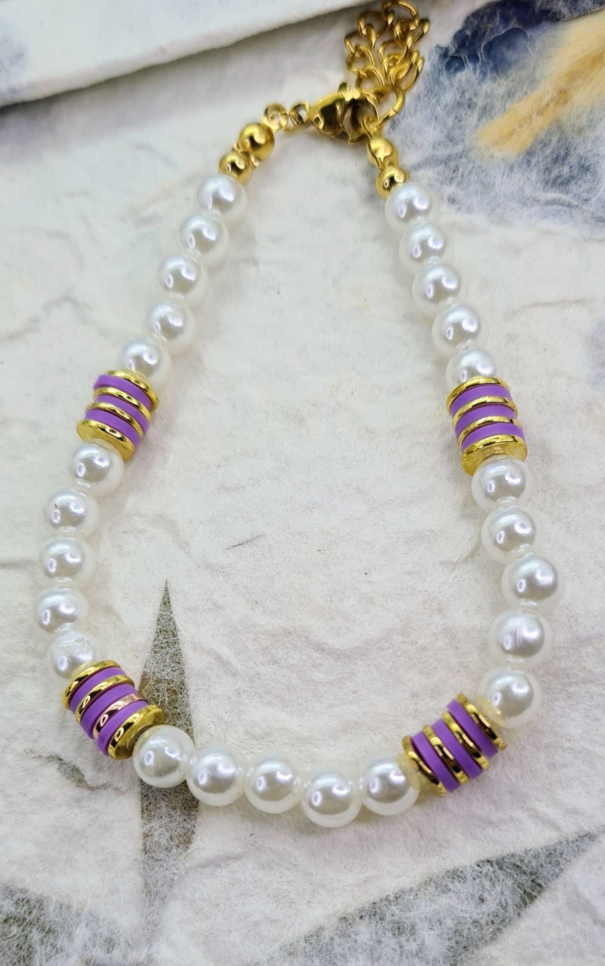 Pulsera completa de perlas blancas con discos de cerámica morados y detalles dorados.