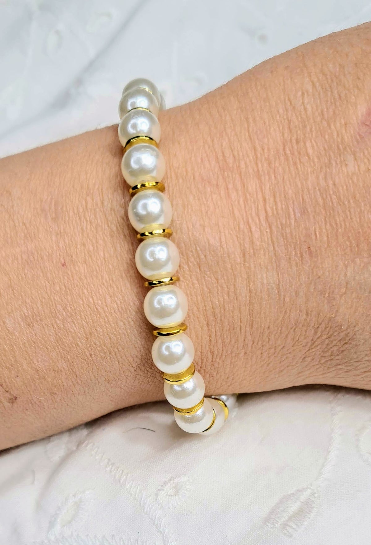 Pulsera de perlas blancas y discos dorados llevada en la muñeca.