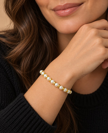 Pulsera de perlas blancas y discos dorados llevada en la muñeca.