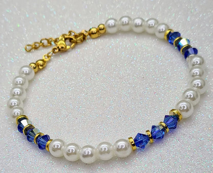 Pulsera de perlas blancas con cristales azules facetados y detalles dorados vista completa.