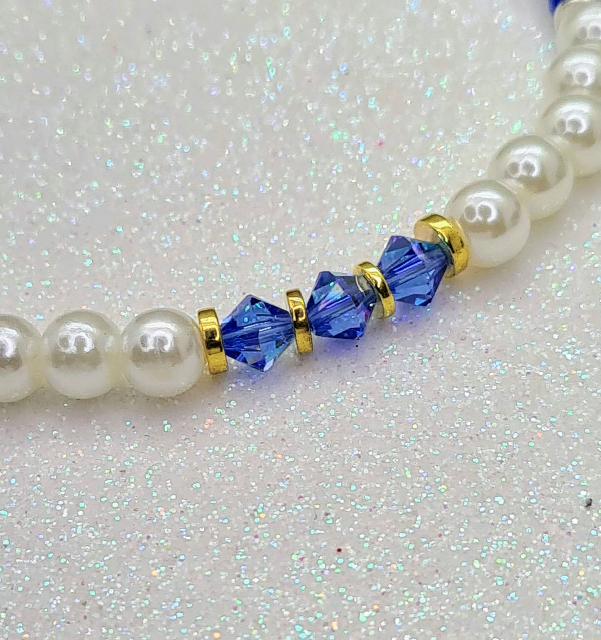 Detalle de perlas blancas, cristales azules facetados y pequeños separadores dorados.
