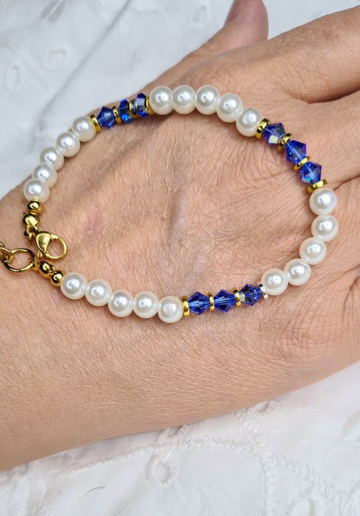 Pulsera de perlas blancas y cristales azules sostenida sobre una mano para mostrar su tamaño.