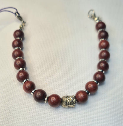 Pulsera de sándalo con Buda central, separadores plateados y extensión sobre fondo claro.