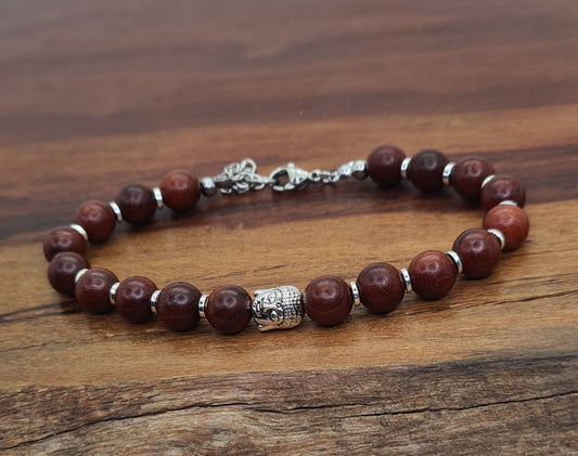 Pulsera unisex de cuentas de sándalo marrón con pieza central de Buda y separadores plateados sobre madera.