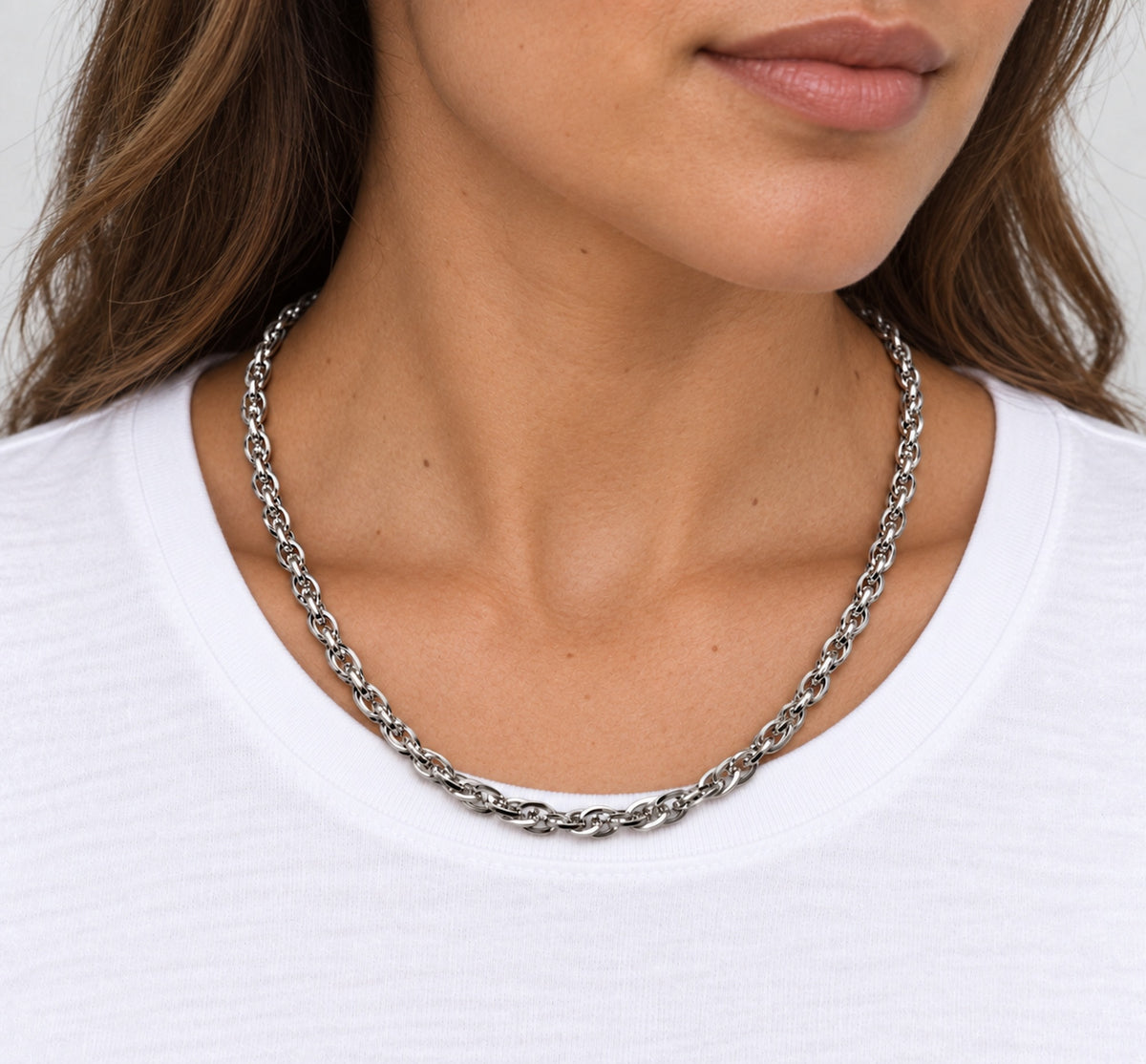 Cadena trenzada de acero llevada alrededor del cuello de una mujer sobre camiseta blanca.