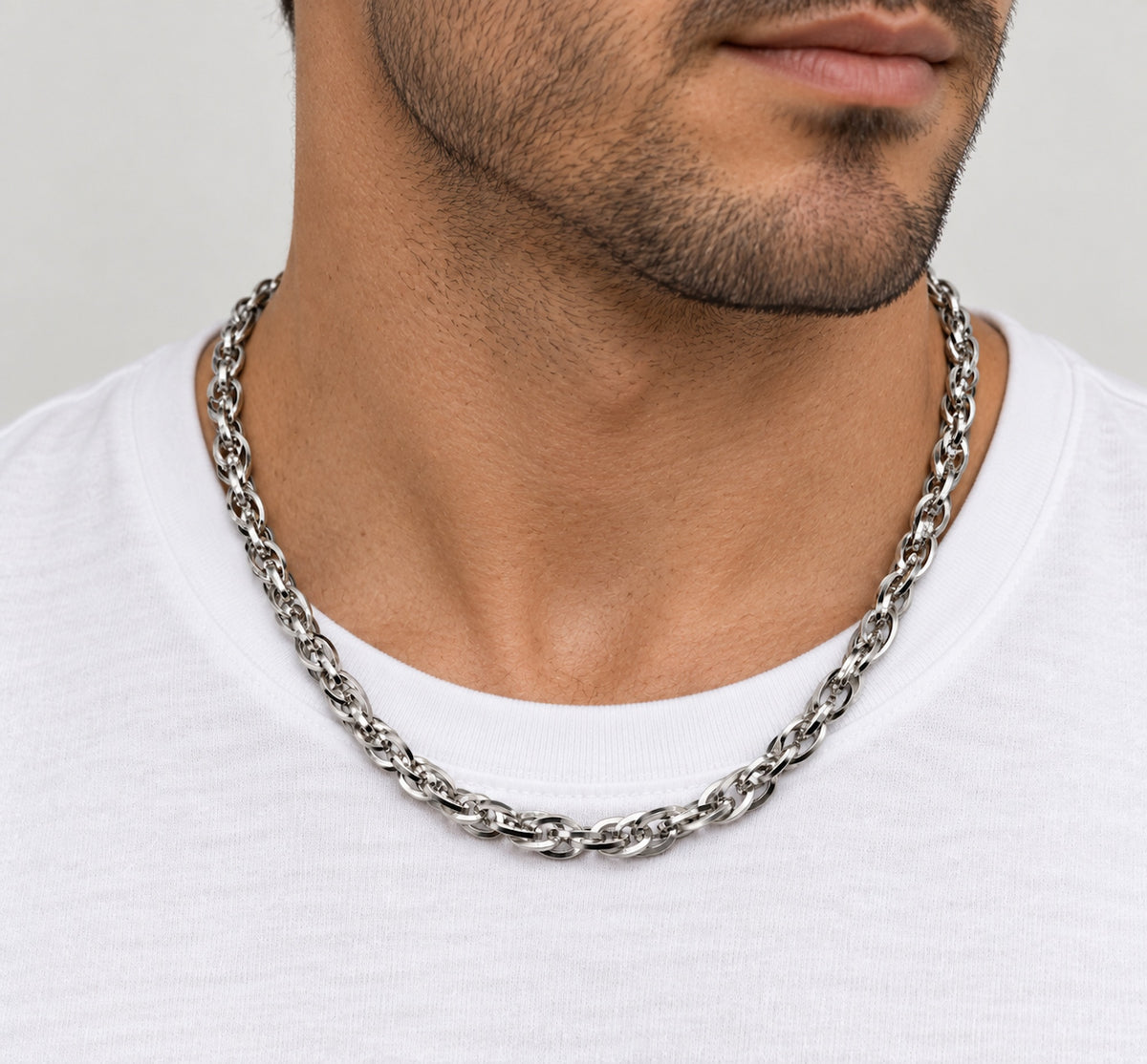 Cadena trenzada de acero alrededor del cuello de un hombre sobre camiseta blanca.